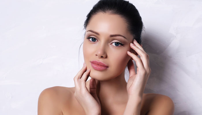 Woman posing with her hands beside her face against a pale background.